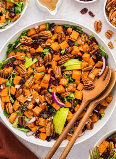 Sweet potato salad in a serving bowl made with cinnamon roasted sweet potatoes and pecans, crumbled bacon, sliced apples, Craisins, mixed greens, feta cheese, and sliced red onions. Served with a maple vinaigrette.