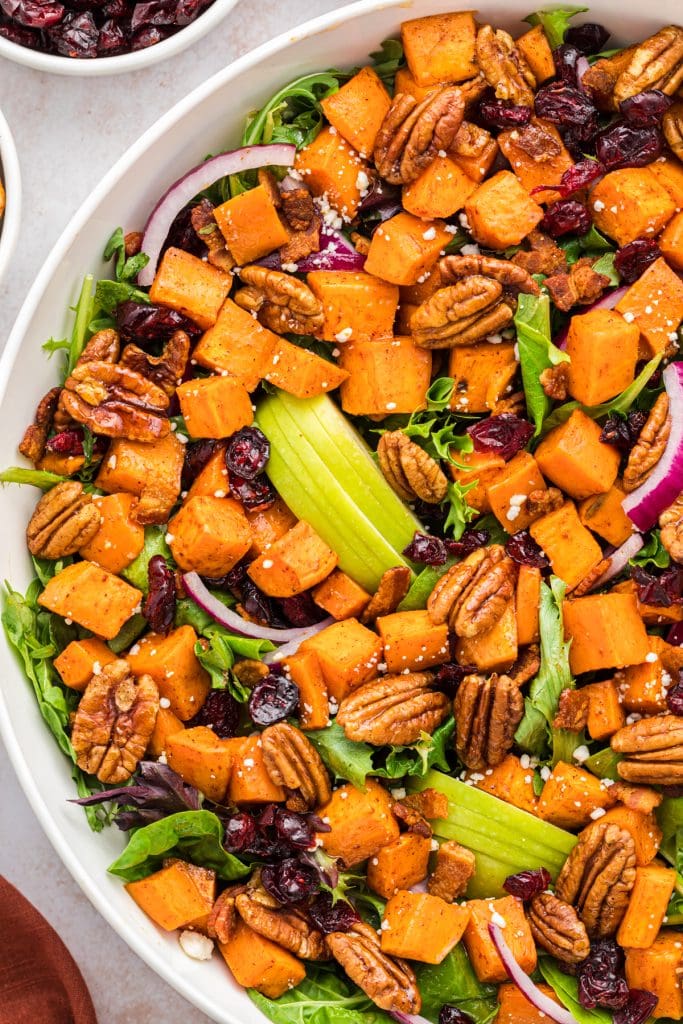 Sweet potato salad in a serving bowl made with cinnamon roasted sweet potatoes and pecans, crumbled bacon, sliced apples, Craisins, mixed greens, feta cheese, and sliced red onions. Served with a maple vinaigrette.