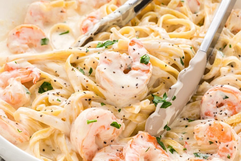 This Creamy Fettuccine Alfredo with Shrimp is a classic recipe with cream, Parmesan, butter, garlic, and shrimp. Here the Creamy Fettuccine Alfredo with Shrimp is served in a large bowl with tongs in the middle ready to serve the pasta.