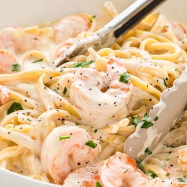 This Creamy Fettuccine Alfredo with Shrimp is a classic recipe with cream, Parmesan, butter, garlic, and shrimp. Here the Creamy Fettuccine Alfredo with Shrimp is served in a large bowl with tongs in the middle ready to serve the pasta.
