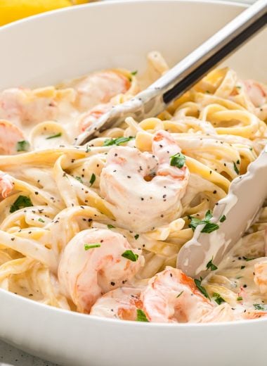 This Creamy Fettuccine Alfredo with Shrimp is a classic recipe with cream, Parmesan, butter, garlic, and shrimp. Here the Creamy Fettuccine Alfredo with Shrimp is served in a large bowl with tongs in the middle ready to serve the pasta.