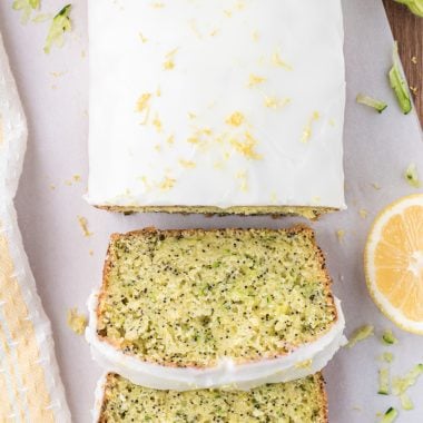 This moist, lemon zucchini poppy seed bread includes a lemon pudding mix, yogurt, shredded zucchini, lemon zest, and poppy seed in its ingredients. This delicious bread is covered in a creamy icing that has a touch of almond extract. Here is a picture of an overhead shot of the loaf with the first two pieces sliced.