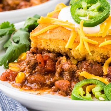 This Chili and Cornbread Casserole made with homemade chili seasoned with ground beef, chili beans, green chiles, broth, tomatoes, seasonings, and corn, and topped with a cornbread mix is an easy and delicious weeknight meal. We love the cornbread chili ratio and the slightly sweet cornbread combined with the flavorful seasoned chili. This casserole is tasty, healthy, comfort food sure to please kids and adults alike, it is a tried and true family favorite! Here it is pictured served on a dinner plate and garnished with sour cream, shredded cheese, sliced jalapeño and cilantro.