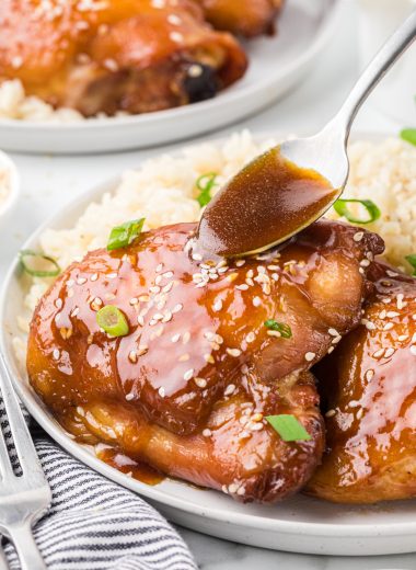 This Brown Sugar Soy Chicken has a simple marinade of brown sugar, soy sauce, butter, water, and seasoning. Part of the marinade is reserved as a glaze for the chicken after it bakes. Whether you marinate it for two or twenty-four hours, the chicken has tremendous flavor. This baked chicken is easy to prepare and is a perfect weeknight meal. Here the chicken is served on a plate with a side of rice with a spoon glazing the chicken with the reserved sauce.