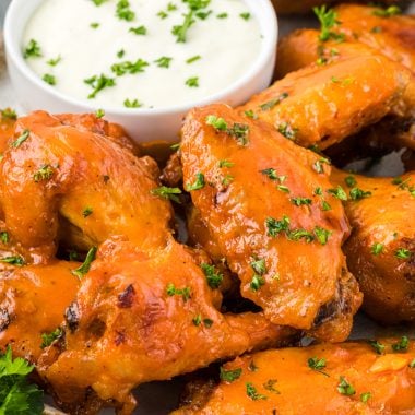 These flavorful Buffalo Honey Wings are baked and then glazed with a honey buffalo sauce that takes these wings over the top. The honey slightly mellows the hot sauce and adds amazing flavor; you really can't eat just one. These are delicious with your favorite blue cheese or ranch dip and are the perfect addicting appetizer for Game Day or your next gathering. Here are the wings are on a serving plate with blue cheese dressing on the side.