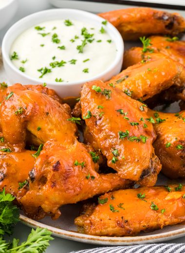 These flavorful Buffalo Honey Wings are baked and then glazed with a honey buffalo sauce that takes these wings over the top. The honey slightly mellows the hot sauce and adds amazing flavor; you really can't eat just one. These are delicious with your favorite blue cheese or ranch dip and are the perfect addicting appetizer for Game Day or your next gathering. Here are the wings are on a serving plate with blue cheese dressing on the side.