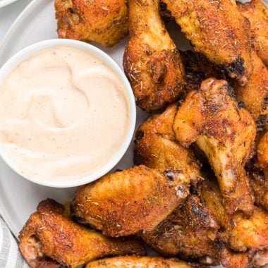 These flavorful baked Cajun Chicken Wings have a Cajun rub and glaze. The remoulade sauce is mayonnaise-based with mustard, pickle juice, garlic, ketchup, hot sauce, Cajun seasoning, and Worcestershire sauce. I have my own Cajun seasoning listed in the recipe, all with pantry ingredients, or you can use one from the store. Here the wings are pictured on a serving plate with a small bowl of remoulade sauce