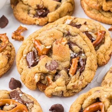 We love that these Chocolate Chip Pretzel Cookies have the perfect balance of sweet and salty. Loaded with chocolate chips, chocolate chunks, and pretzels, every bite has an addicting chocolately-salty crunch. These are a favorite family cookie that always disappear in a flash. Here the cookies are paired in twos or threes and displayed on parchment paper with pretzel pieces, chocolate chips and a glass of m.ilk