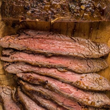 This Marinated Flank Steak Recipe with soy sauce, lime and orange juice, cilantro, garlic, chipotle, and seasonings makes an incredibly tender and flavorful steak. Cooked quickly under the broiler or on the grill, this steak tastes amazing on its own or served in tacos, fajitas, bowls, or salads. Here the steak is displayed on a cutting board with several slices cut in front of it.
