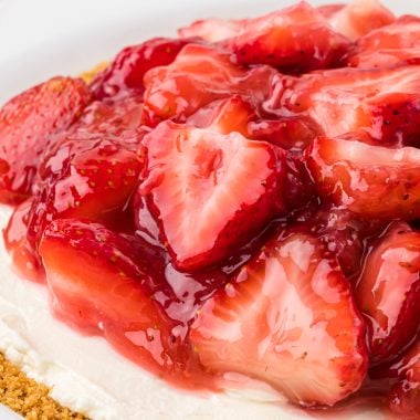This Cream Cheese and Strawberry Pie has a graham cracker crust, a no-bake cream cheese filling, and a sweet homemade strawberry pie topping. It is an easy dessert, perfect for the summer holidays, and is a favorite at family gatherings. Here the whole pie is at the center of the image, prepared to serve, with the the focal point on the strawberry filling.
