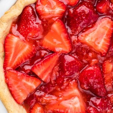 This Strawberry Glazed Pie is a favorite summer tradition. Fresh strawberries, generously piled into a homemade or store-bought crust, combined with a sweetened fresh strawberry glaze, topped with a generous dollop of whipped cream, make the ultimate summer dessert. Here the pie is pictured in an overhead shot of the whole pie, filled and ready to serve.