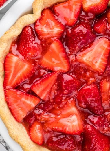 This Strawberry Glazed Pie is a favorite summer tradition. Fresh strawberries, generously piled into a homemade or store-bought crust, combined with a sweetened fresh strawberry glaze, topped with a generous dollop of whipped cream, make the ultimate summer dessert. Here the pie is pictured in an overhead shot of the whole pie, filled and ready to serve.