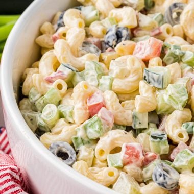 This Vegetable Macaroni Salad is a favorite side for family barbecues and potlucks. Made with a creamy mayo dressing and filled with olives, cucumbers, celery, tomatoes, dill pickles, green onions, and pimientos, this flavor-packed pasta salad has a perfect blend of crispness from the veggies and creaminess from the dressing. Here the image is close up on the serving bowl filled with the macaroni salad, ready to serve.