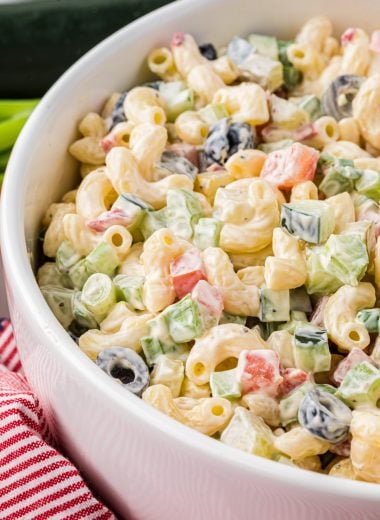 This Vegetable Macaroni Salad is a favorite side for family barbecues and potlucks. Made with a creamy mayo dressing and filled with olives, cucumbers, celery, tomatoes, dill pickles, green onions, and pimientos, this flavor-packed pasta salad has a perfect blend of crispness from the veggies and creaminess from the dressing. Here the image is close up on the serving bowl filled with the macaroni salad, ready to serve.
