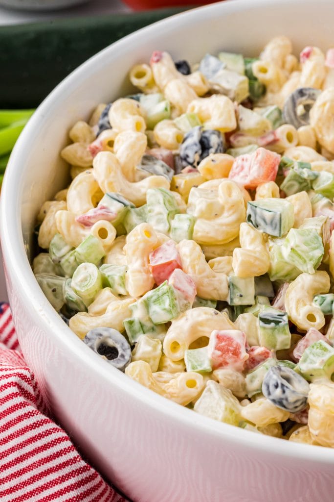 This Vegetable Macaroni Salad is a favorite side for family barbecues and potlucks. Made with a creamy mayo dressing and filled with olives, cucumbers, celery, tomatoes, dill pickles, green onions, and pimientos, this flavor-packed pasta salad has a perfect blend of crispness from the veggies and creaminess from the dressing. Here the image is close up on the serving bowl filled with the macaroni salad, ready to serve.