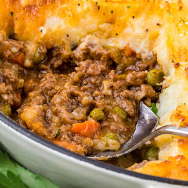 This Cottage Pie with Cheese (also known as Shepherd's Pie) has creamy Parmesan crusted mashed potatoes over a rich and flavorful beef and vegetable filling. The buttery mashed potatoes, enhanced with cream and additional Parmesan, are amazing on their own, but combined with the savory beef filling with gravy make the perfect comfort food. Here the shepherd's pie is featured with a serving cut out and a spoon in the center of the image filled with the beef filling.
