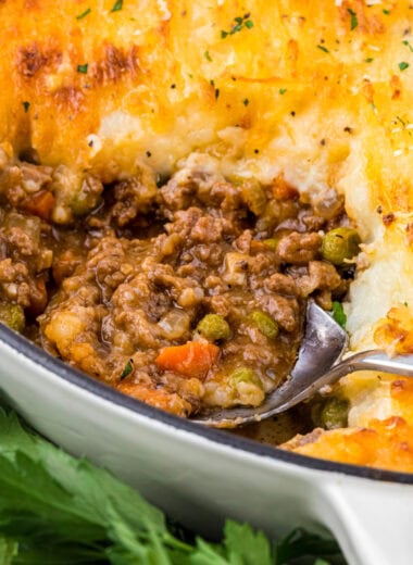 This Cottage Pie with Cheese (also known as Shepherd's Pie) has creamy Parmesan crusted mashed potatoes over a rich and flavorful beef and vegetable filling. The buttery mashed potatoes, enhanced with cream and additional Parmesan, are amazing on their own, but combined with the savory beef filling with gravy make the perfect comfort food. Here the shepherd's pie is featured with a serving cut out and a spoon in the center of the image filled with the beef filling.