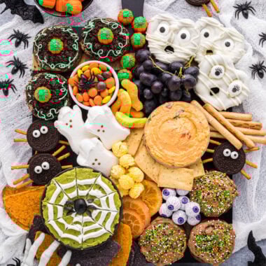 This Halloween Themed Charcuterie Board is as much fun to see as it is to eat. This kid-friendly snack board is filled with sweet and savory Halloween treats, and has a playful mix of spooky, silly, and sweet. The recipes for the cookies, mummy pretzels, and spider web dip are in the blog post as well as lots of tips for how to create a charcuterie board. This board is easy to customize and is a favorite at any Halloween table, party, or gathering. This overhead shot of the board shows Pumpkin Patch Cookies, Chocolate Frosted Cookies, Mummy Pretzels, and a Spider Web dip in each corner of the board. The board is filled with Oreo Spider Cookies, a pimento cheese dip, grapes, cheddar popcorn, dried oranges, Halloween chips, pretzels, pita chips, gummy worms, marshmallow ghosts, candy pumpkins, and candy eyeballs.