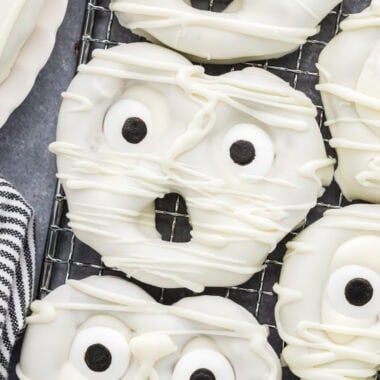 These Mummy Pretzels are a fun and spooky Halloween treat. With just three ingredients, they are an easy, no-bake snack that kids love to help make and eat. Their cute faces and delicious sweet and salty combination make them the perfect treat for a Halloween celebration, class party, movie night, or goodie bag. The overhead shot here shows the pretzels close together on a cooling rack