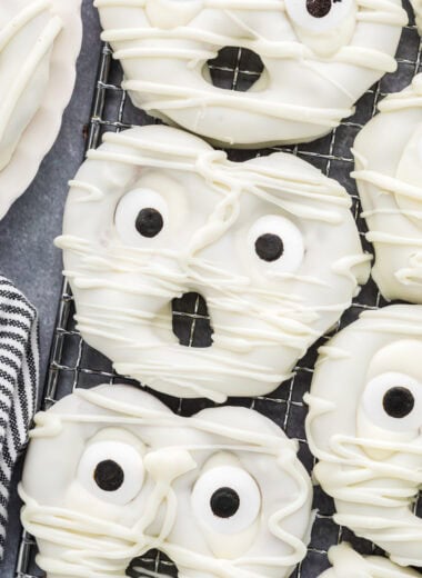 These Mummy Pretzels are a fun and spooky Halloween treat. With just three ingredients, they are an easy, no-bake snack that kids love to help make and eat. Their cute faces and delicious sweet and salty combination make them the perfect treat for a Halloween celebration, class party, movie night, or goodie bag. The overhead shot here shows the pretzels close together on a cooling rack