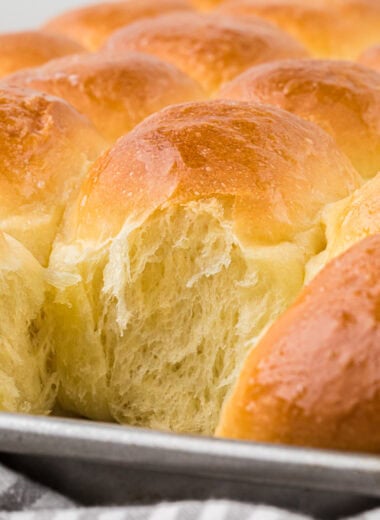 These Big Soft Fluffy Dinner Rolls are a favorite at our dinner table. Irresistibly soft on the inside with a buttery golden crust, this recipe makes a big batch of 35 rolls at once, making it a perfect side for holiday and family dinners. Here the rolls are on the baking sheet hot out of the oven. One roll has been taken off and the shot shows the fluffiness of the rolls in the pan.