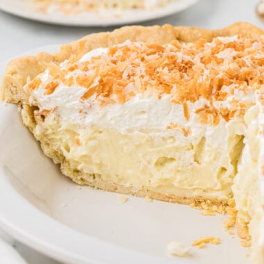 This Coconut Cream Pie with Coconut Milk, made with part coconut milk and half-and half, is my husband's favorite pie. We have made it for countless birthdays and holidays, and truthfully, it is always a favorite for guests and family. It has a dreamy, creamy custard with coconut flavor that shines through from the coconut milk, sweetened coconut flakes in the custard, and toasted coconut flakes sprinkled on top. Here the pie is in the pan in the center of the image, and has been sliced into to see the creamy filling of the pie. Slices of the pie are in the background.