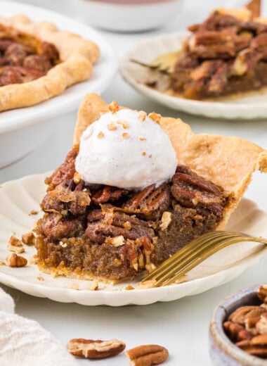 This Maple Pecan Pie without Corn Syrup has the buttery, nutty, gooey filling you expect from pecan pie but with an added depth of flavor from maple syrup. Made with mostly maple syrup, some honey for thickening, and a touch of maple extract, each bite of the pecan pie has a hint of maple which beautifully compliments the roasted, sweetened pecans. Here in the center of the image is a slice of pecan pie with a bite taken out of the front with the pie and an additional slice in the background. Maple syrup and pecans are in the foreground and background as well.
