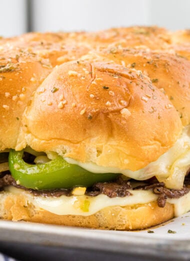 These Philly Cheesesteak Sliders are an irresistible Game Day or party snack with seasoned shaved steak, tender sauteed onions and peppers, creamy melted provolone, a garlic mayo spread, and buttery soft rolls. These gooey, flavorful little sandwiches are perfect for feeding a crowd, and are a huge favorite here. Here the rolls are on the baking sheet straight out of the oven with the corner roll in the center of the frame.