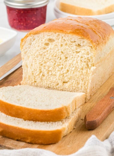 In this image, the bread is on the cutting board, with two slices cut in front of the loaf. It has butter and jam in the background.