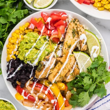 This overhead image has all the bowl ingredients assembled in a bowl, garnished with crema in the center of the image with an additional bowl and other bowl ingredients around it.