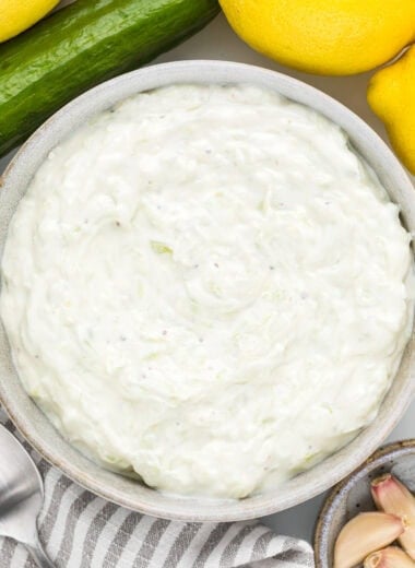 In this overhead image, the tzatziki sauce is in a serving bowl ready to serve with additional cucumber, lemon, and garlic surrounding it.