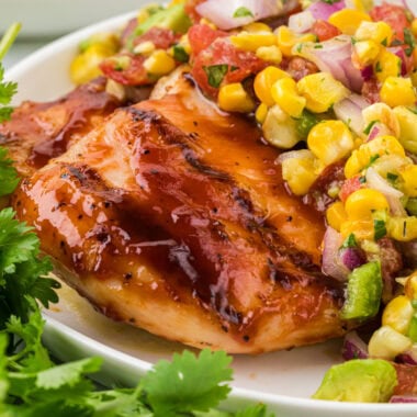 This image shows the barbecue chicken plated in the center with a serving of the roasted corn salsa placed over the center of the chicken.