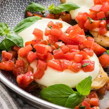 In this image, the cooked chicken is in the pan with melted mozzarella and the tomato mixture spooned on top.