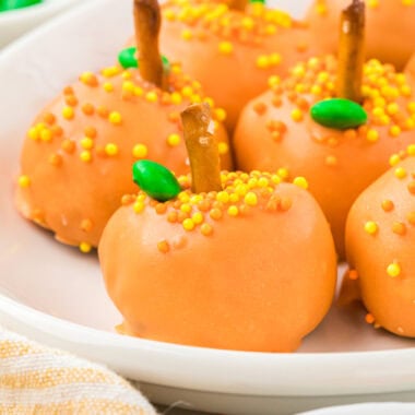 In this image, the pumpkin balls are on an oval platter, with sprinkles, pretzels, and mini-green M&Ms in the foreground and background.